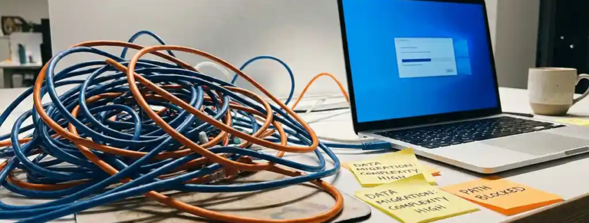 Verward kluwen ethernetkabels op wit bureau naast open laptop, symboliseert complexiteit bij netwerkmigratie.