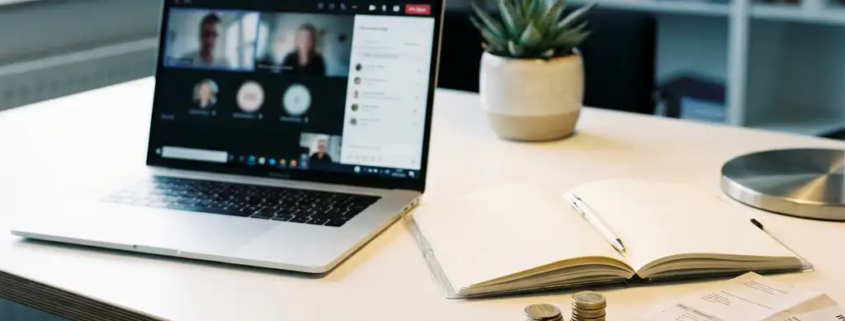 Moderne kantaartafel met laptop met Microsoft Teams, opengeslagen notitieboek, euromuntjes en gevouwen factuur in natuurlijk licht.